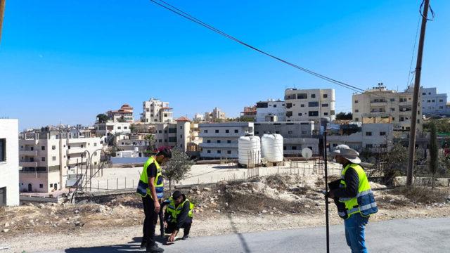 Three men in yellow vests standing on the street in a city holding survey equipment